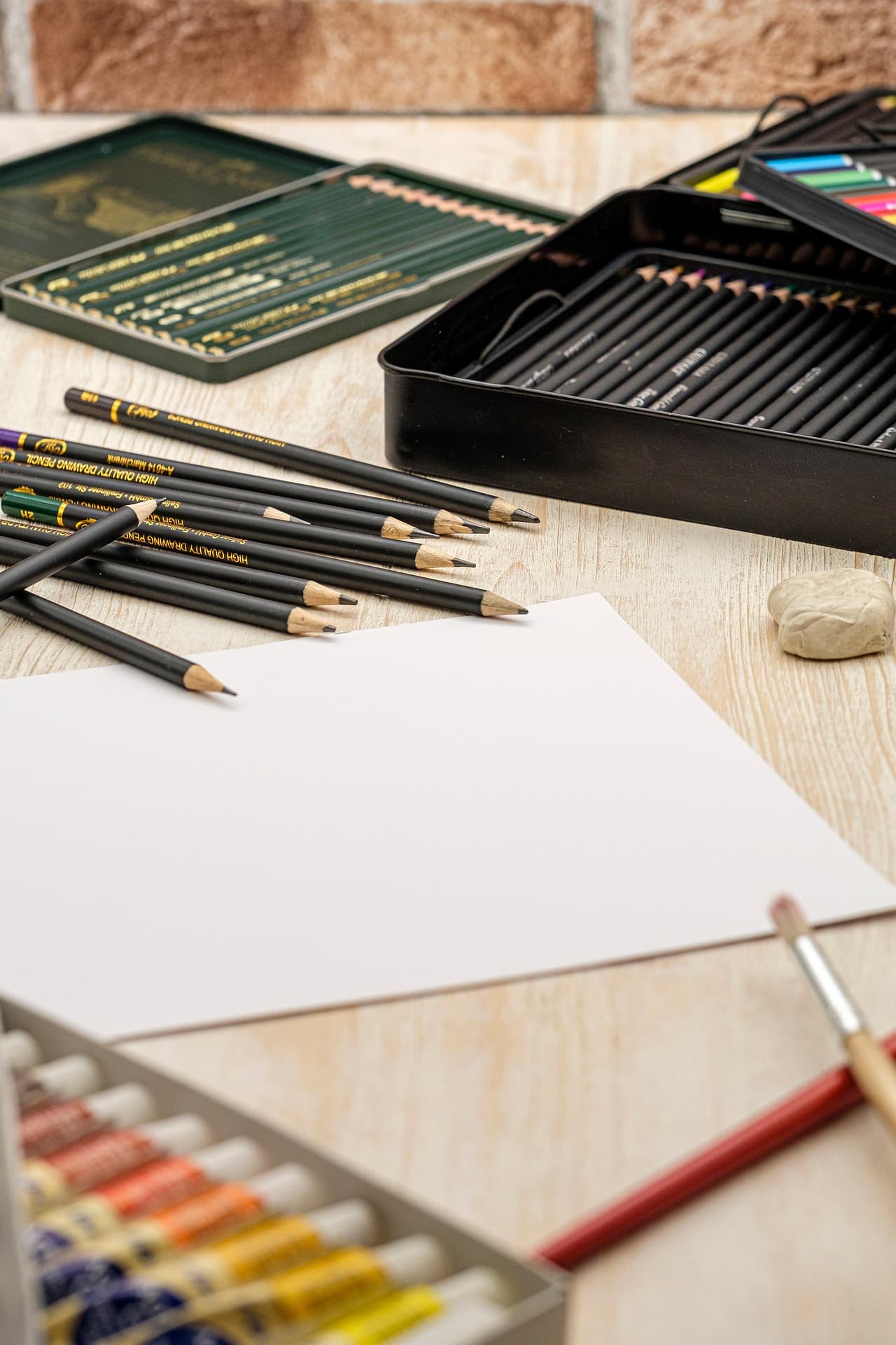 Materiales de dibujo y papelería sobre mesa de madera, con hoja blanca central.