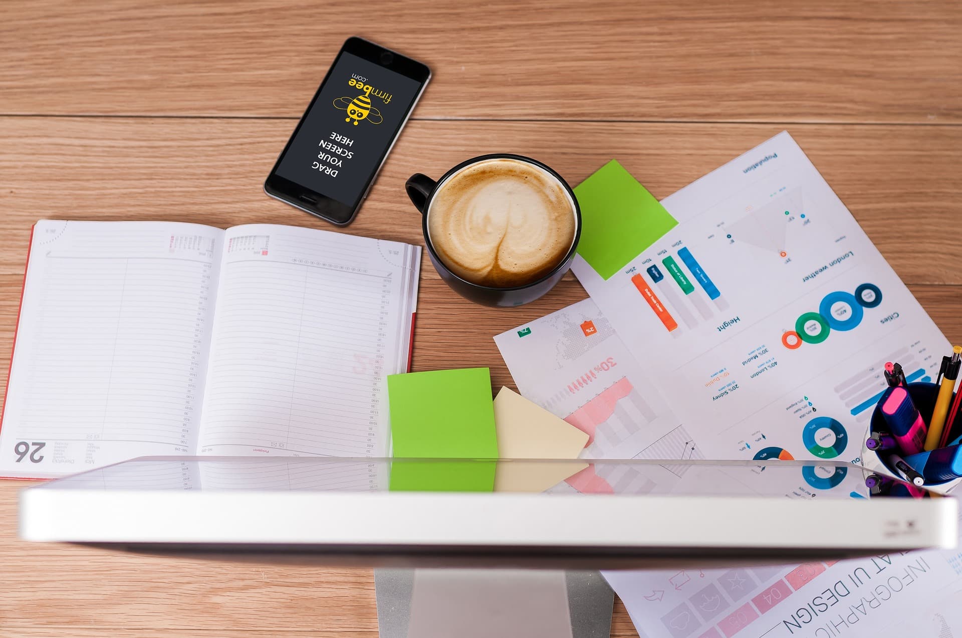 Escritorio con monitor, planner, documentos y artículos de oficina.